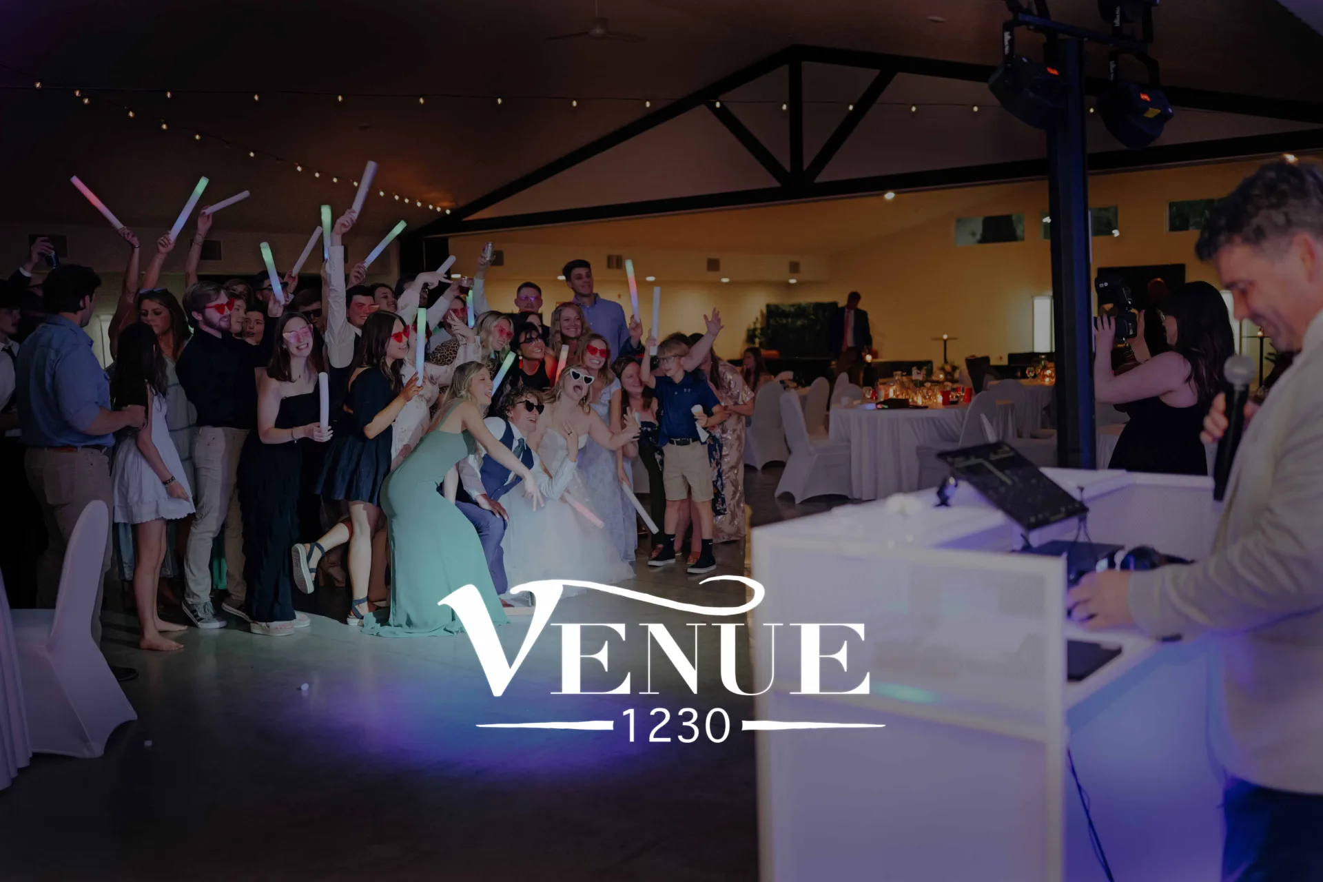 Group of young adults at a nighttime party posing with colorful glow sticks inside a decorated venue.