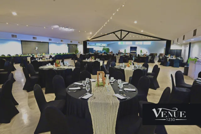 Banquet hall setup with round black-covered tables, elegant centerpieces, and string lights overhead; logo reading Venue 1230 in the corner.