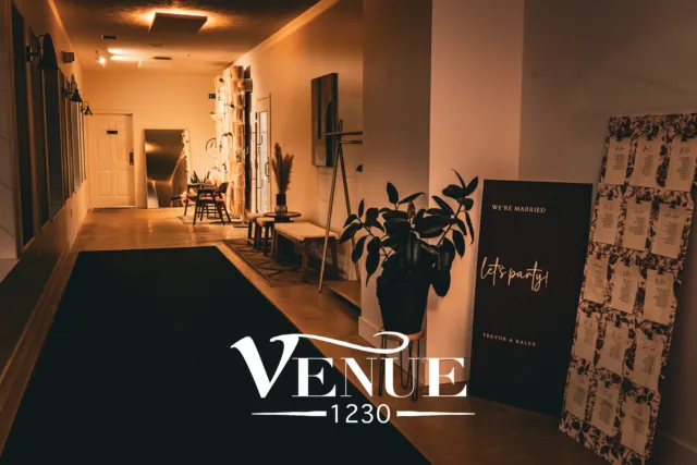 Interior of a warmly lit event venue hallway with seating, plants, and a large 'VENUE' sign in the foreground.